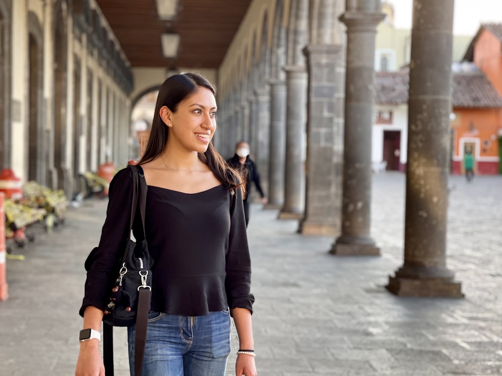 woman in black long sleeve shirt and blue denim jeans standing on sidewalk during daytime