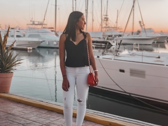 A stylish woman standing on a yacht deck with the ocean and sunset in the background.