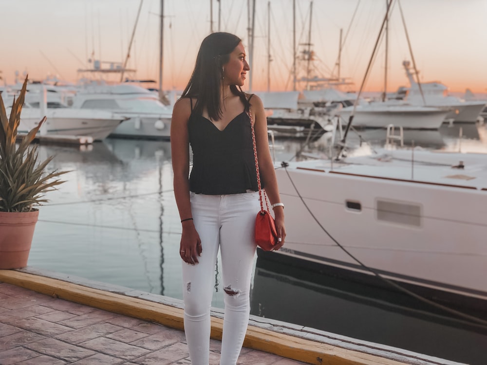 woman in black tank top and white pants standing on dock during daytime
