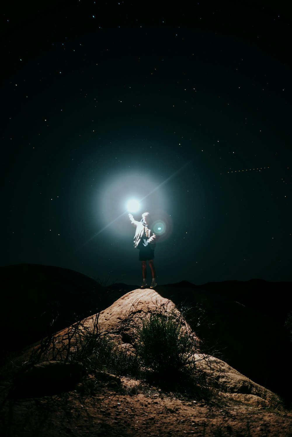 man in black jacket and black pants standing on brown rock during night time