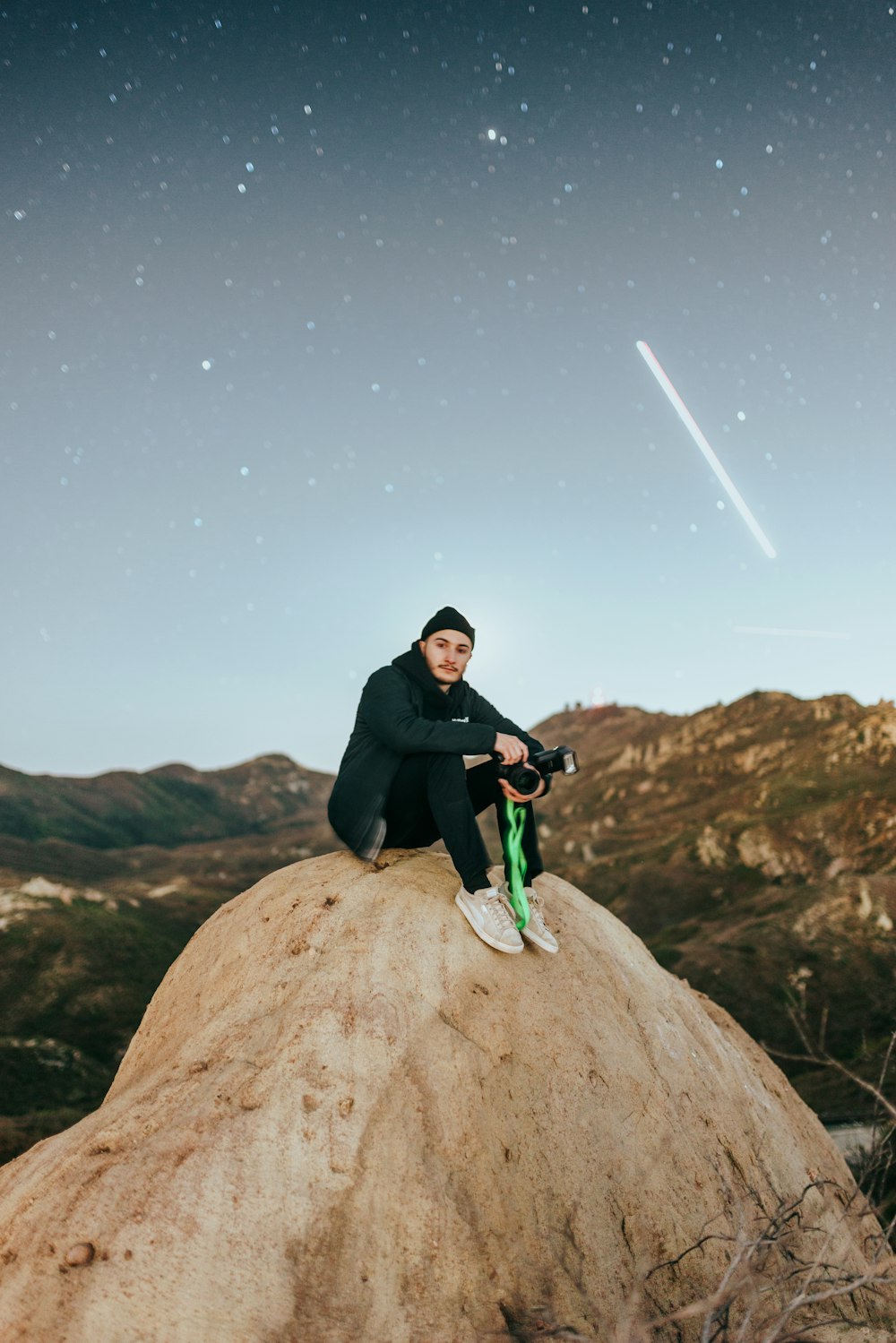 man in black jacket and green pants sitting on brown rock during night time