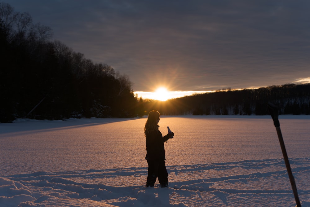 silhouette of person standing on snow covered ground during sunrise