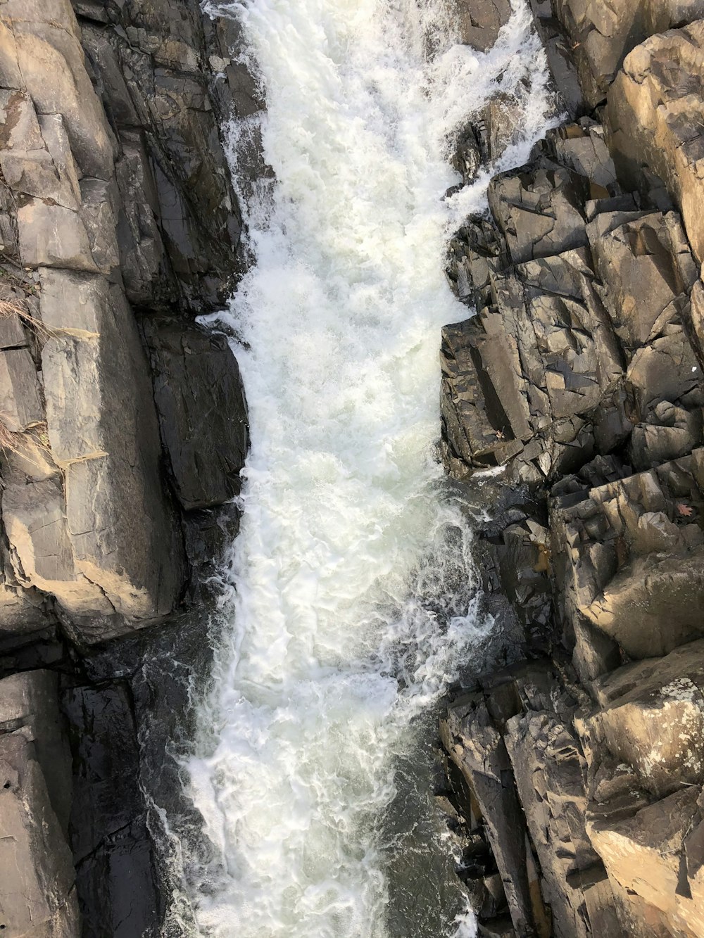 water falls between rocky mountain during daytime