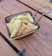A small wire basket filled with triangular crispy snacks is placed on a wooden table. The snacks have a waffle-like texture and are golden brown in color.
