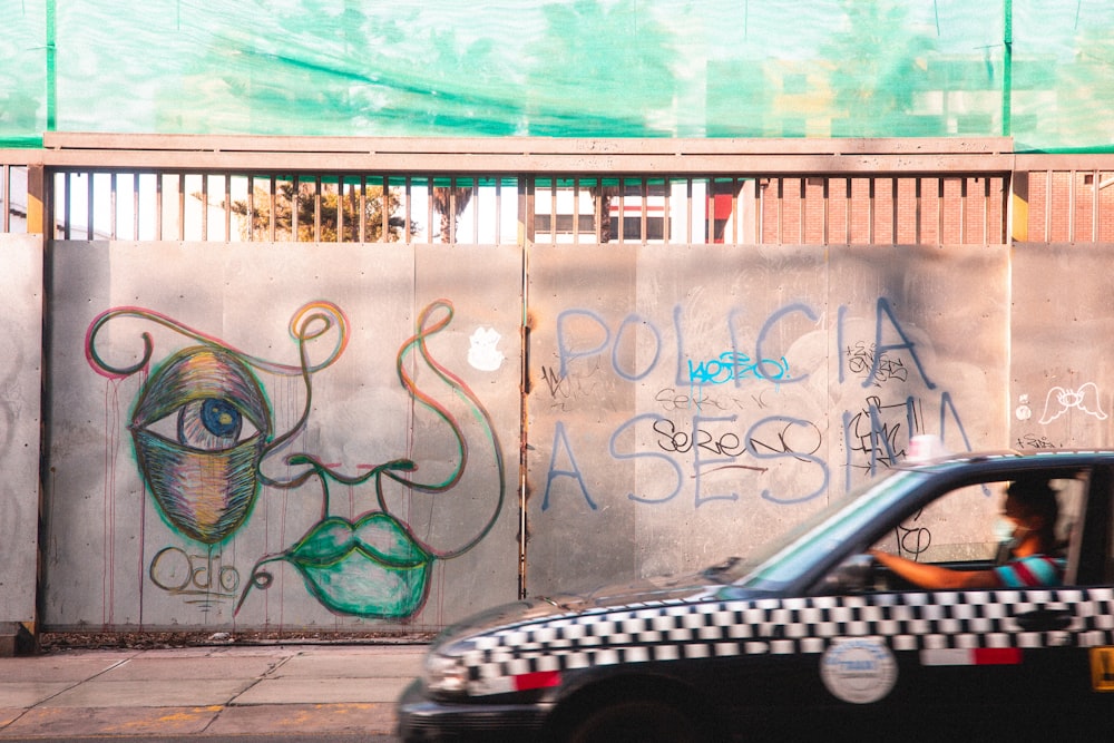 black car parked beside white and blue wall with graffiti