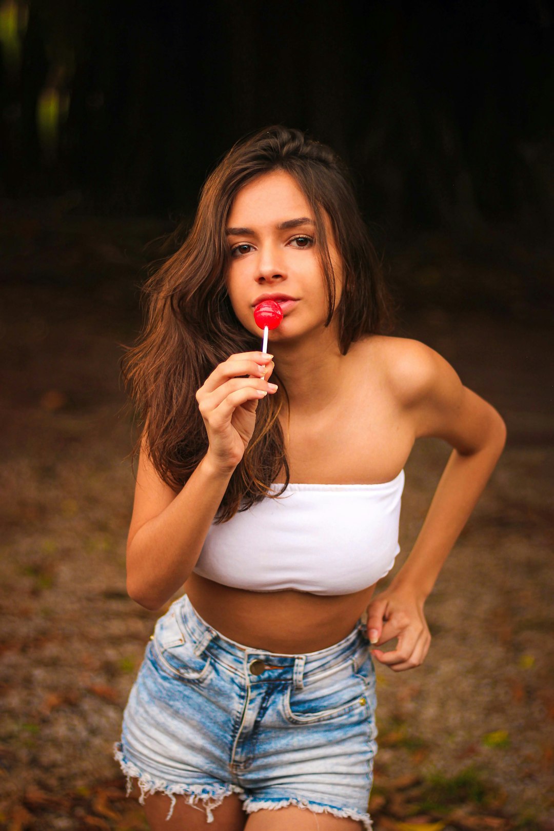woman in white tank top and blue denim shorts holding lollipop