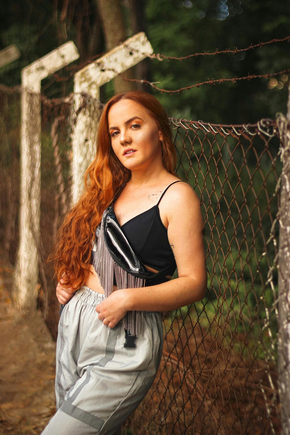 woman in black spaghetti strap top leaning on chain link fence