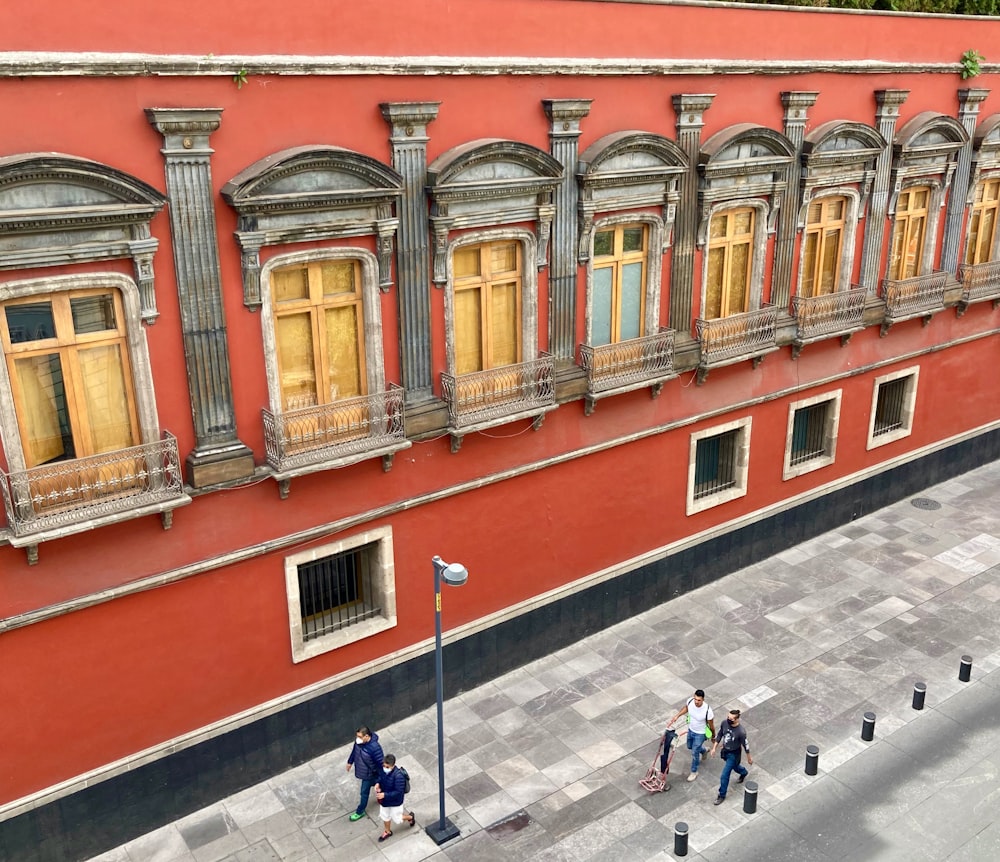 people walking on sidewalk near red and white concrete building during daytime