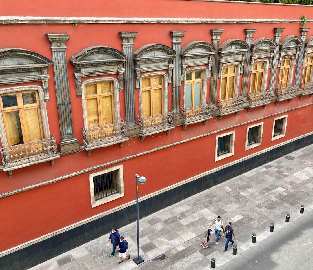 people walking on sidewalk near red and white concrete building during daytime