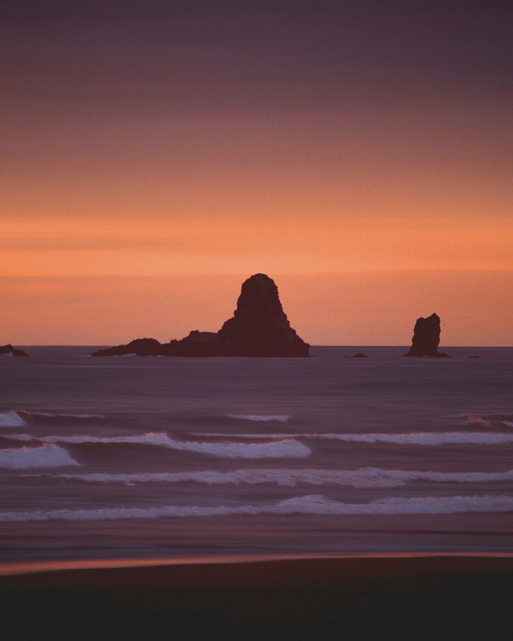 silhueta da formação rochosa no mar durante o pôr do sol