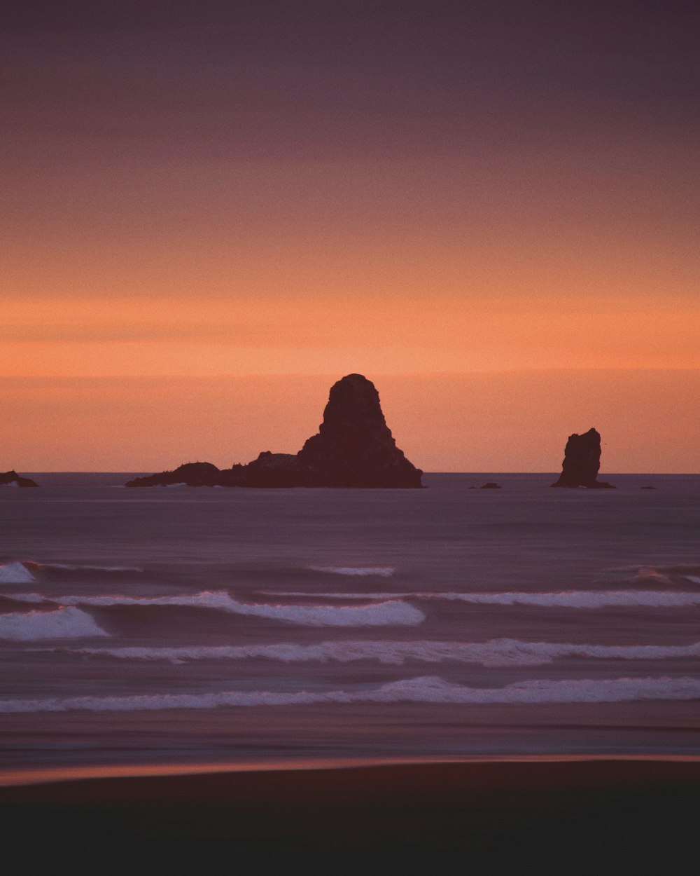 silhouette of rock formation on sea during sunset