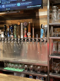 Close-up of custom branded tap handles pouring craft beverages with a backdrop of a glowing menu board.