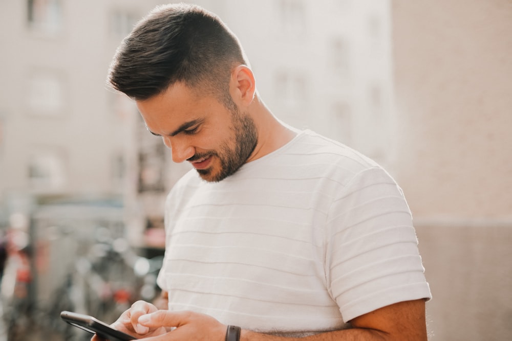 man in white crew neck t-shirt using smartphone