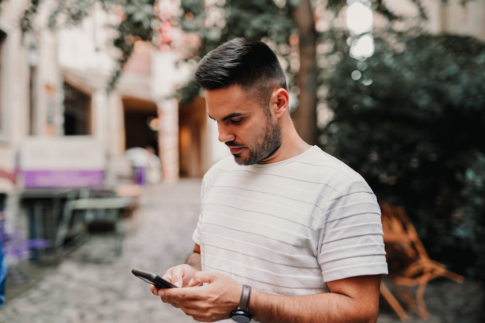 man in white and gray striped polo shirt holding black smartphone