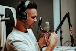 A person wearing headphones is speaking into a professional studio microphone, which is mounted on an adjustable arm. The individual appears focused and engaged with the recording process.