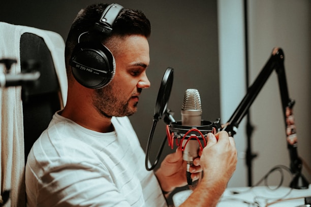 A person wearing headphones is speaking into a professional studio microphone, which is mounted on an adjustable arm. The individual appears focused and engaged with the recording process.