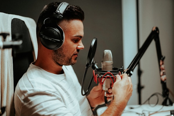 A person wearing headphones is speaking into a professional studio microphone, which is mounted on an adjustable arm. The individual appears focused and engaged with the recording process.