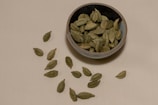 A minimalist flat lay of fresh green cardamom pods resting on a textured terracotta plate.