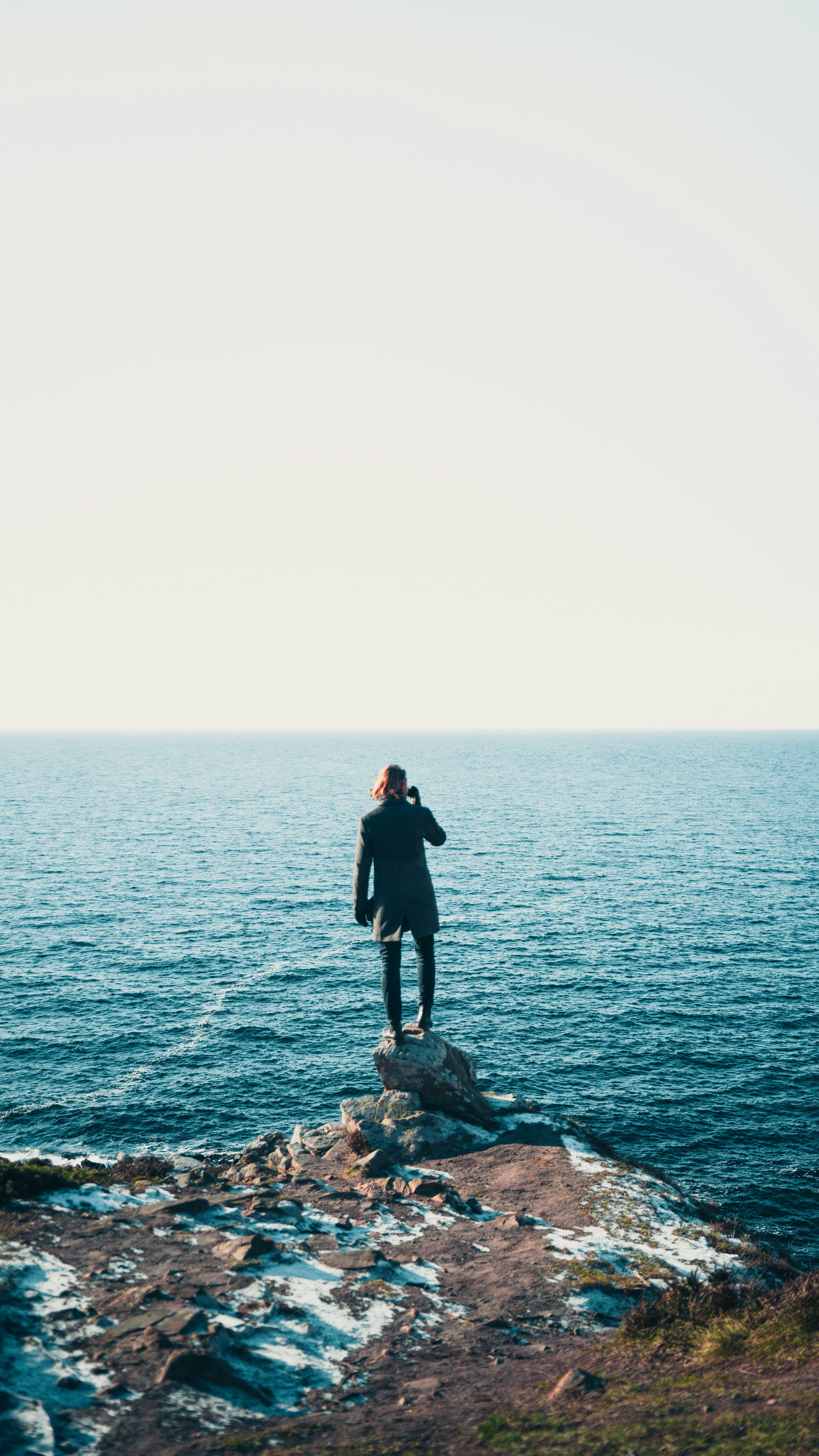 man in black jacket standing on rock formation near sea during daytime
