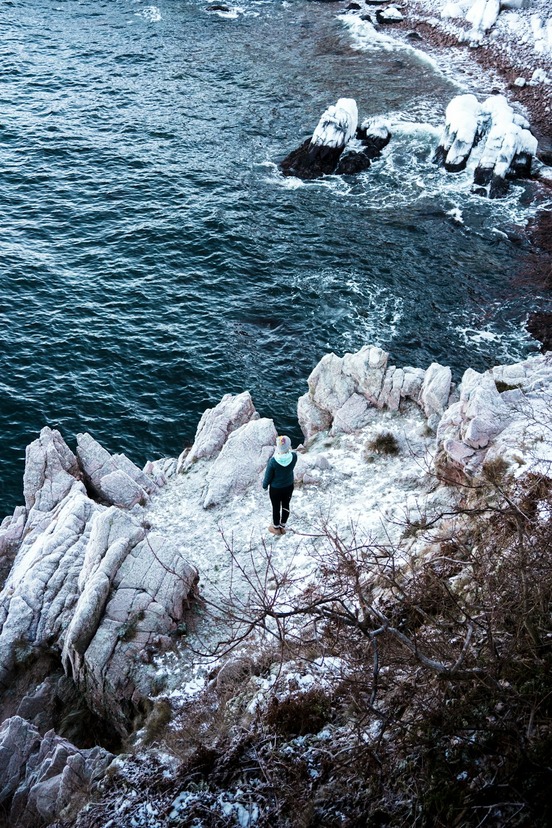 woman in black tank top and blue denim jeans standing on rocky cliff by the sea
