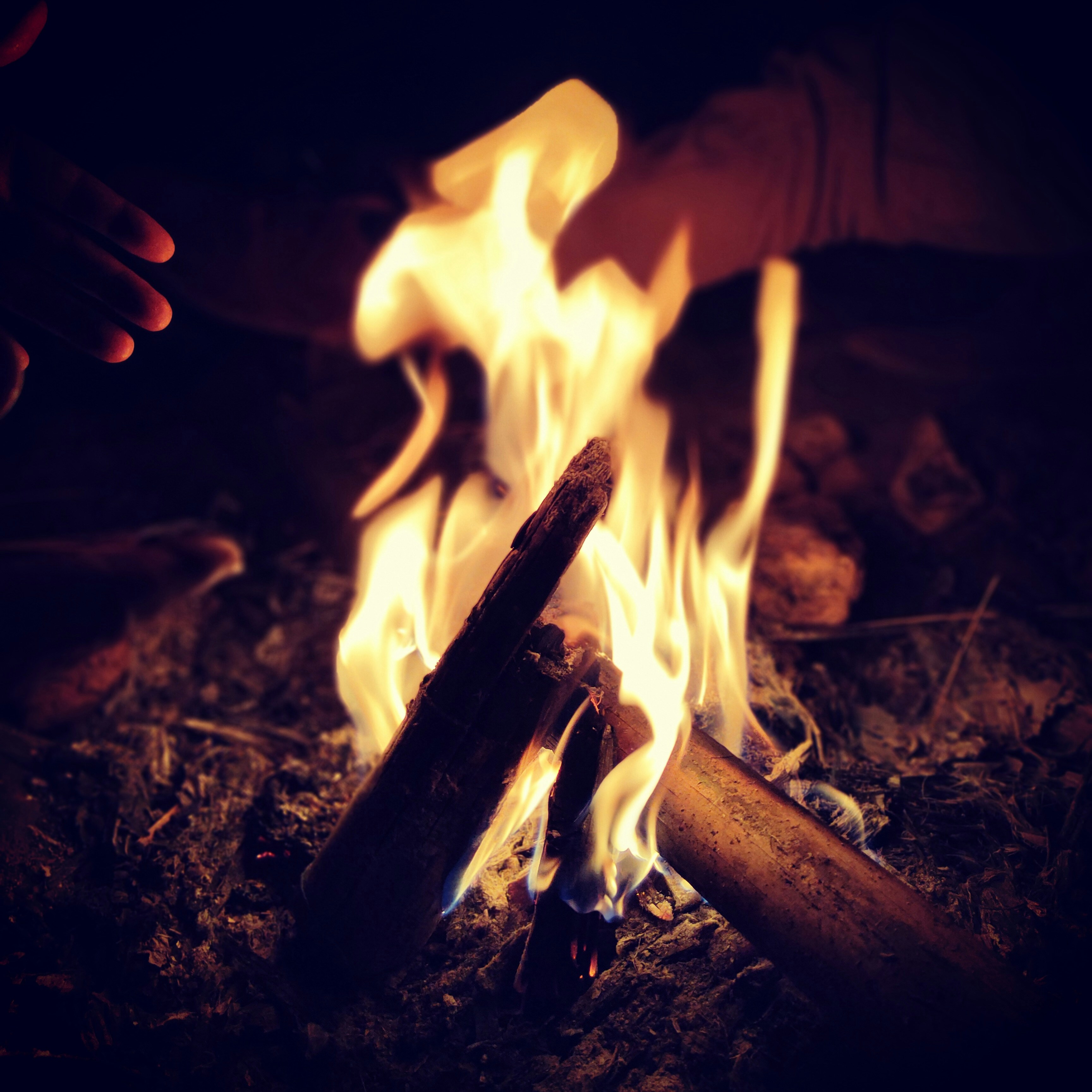 Close-up of a hand lighting a campfire using a Squarefire fire starter with glowing embers.