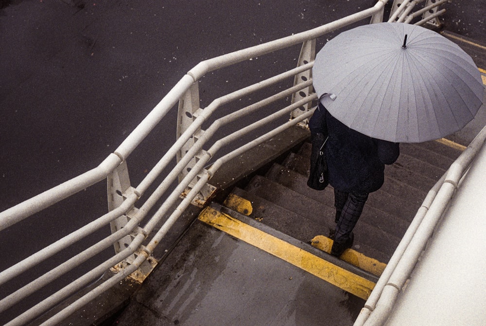 person in black jacket and blue denim jeans holding umbrella walking on staircase