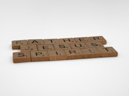 Wooden Scrabble tiles arranged to spell out the words Father, Jesus, and Spirit, placed on a plain white background.