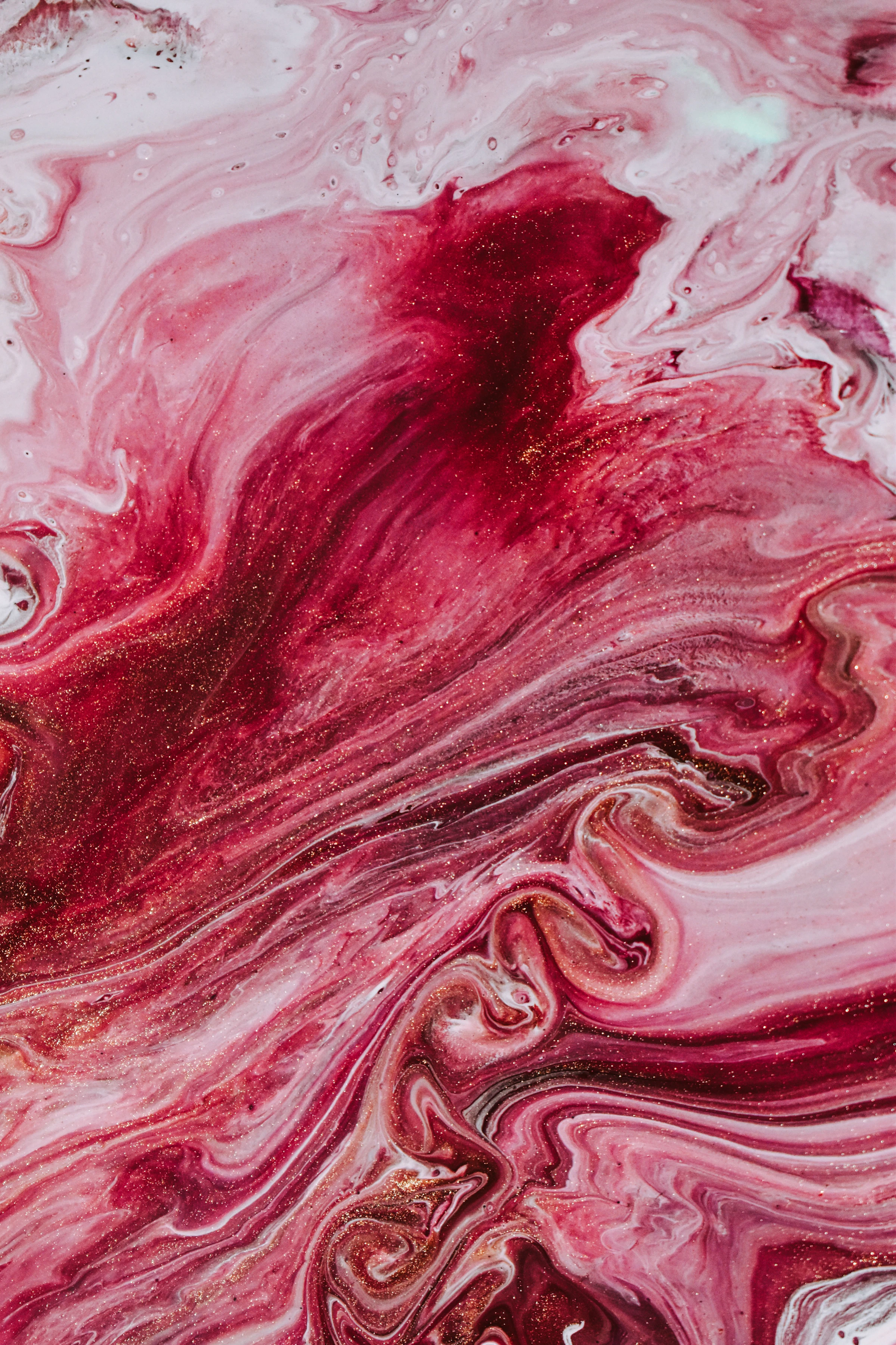 Abstract fluid painting with swirls of red, pink, and white paint and gold glitter