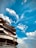 A multi-story building with signage is seen against the backdrop of a bright blue sky with scattered clouds. The building has curved balconies with glass railings and some greenery is present on the upper floors. Notable signage includes 'AVALON BE...' and 'Highla...'.