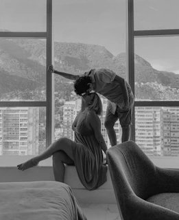 A cinematic capture of a couple sharing a quiet moment by a window with charcoal shadows.