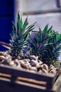 A wooden crate filled with fresh pineapples and ginger roots, illuminated by soft lighting that accentuates the rich green of the pineapple leaves and the earthy tones of the ginger. The background is slightly blurred, emphasizing the produce.