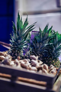 A wooden crate filled with fresh pineapples and ginger roots, illuminated by soft lighting that accentuates the rich green of the pineapple leaves and the earthy tones of the ginger. The background is slightly blurred, emphasizing the produce.