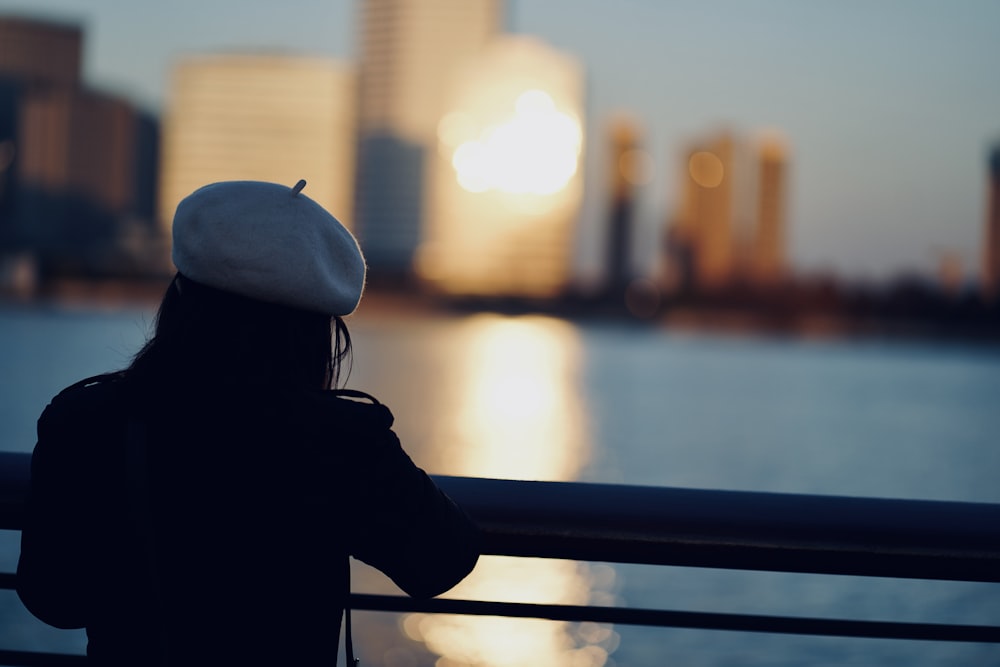 woman in black jacket and white cap standing near blue railings during daytime