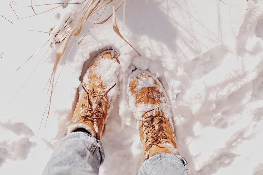 pessoa em sapatos de caminhada marrom em pé no chão coberto de neve