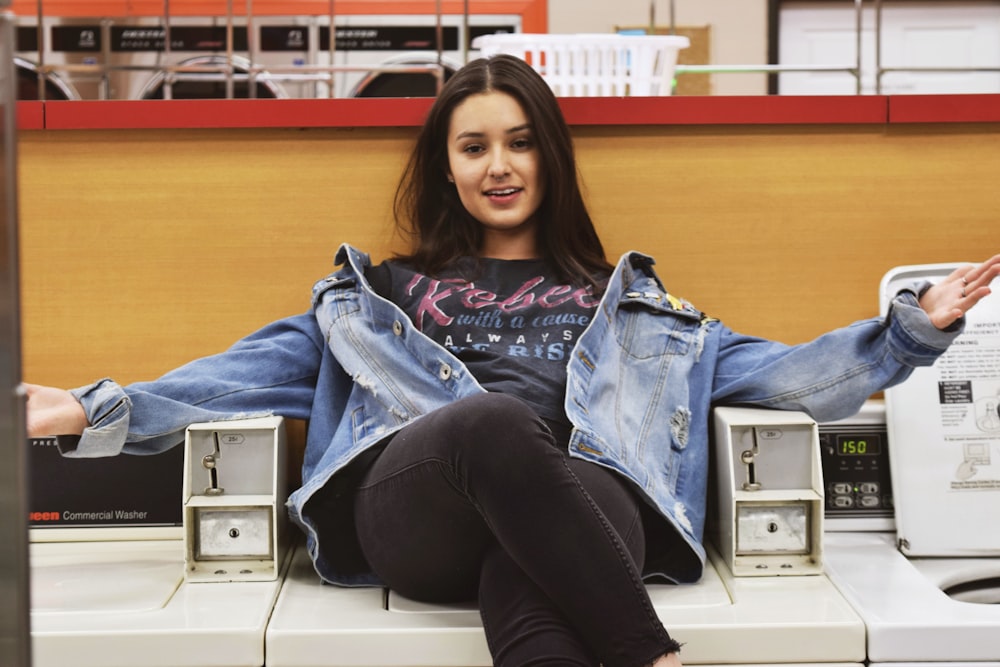 woman in blue denim jacket and black pants sitting on white table