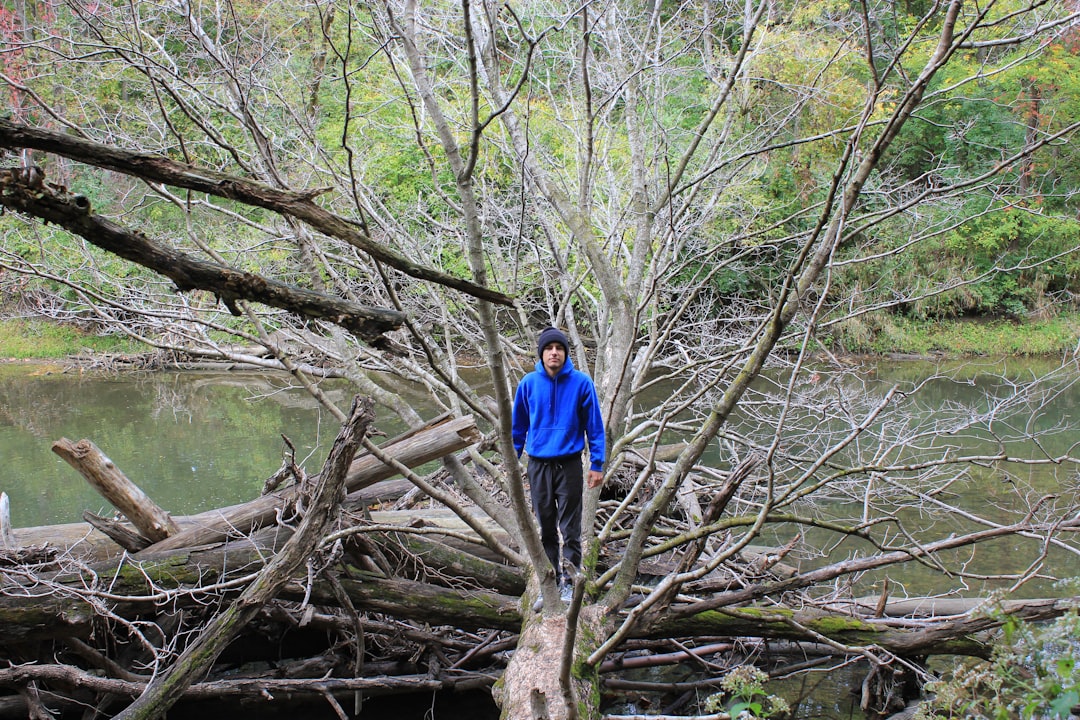 woman in blue jacket and blue denim jeans standing on brown tree log on river during