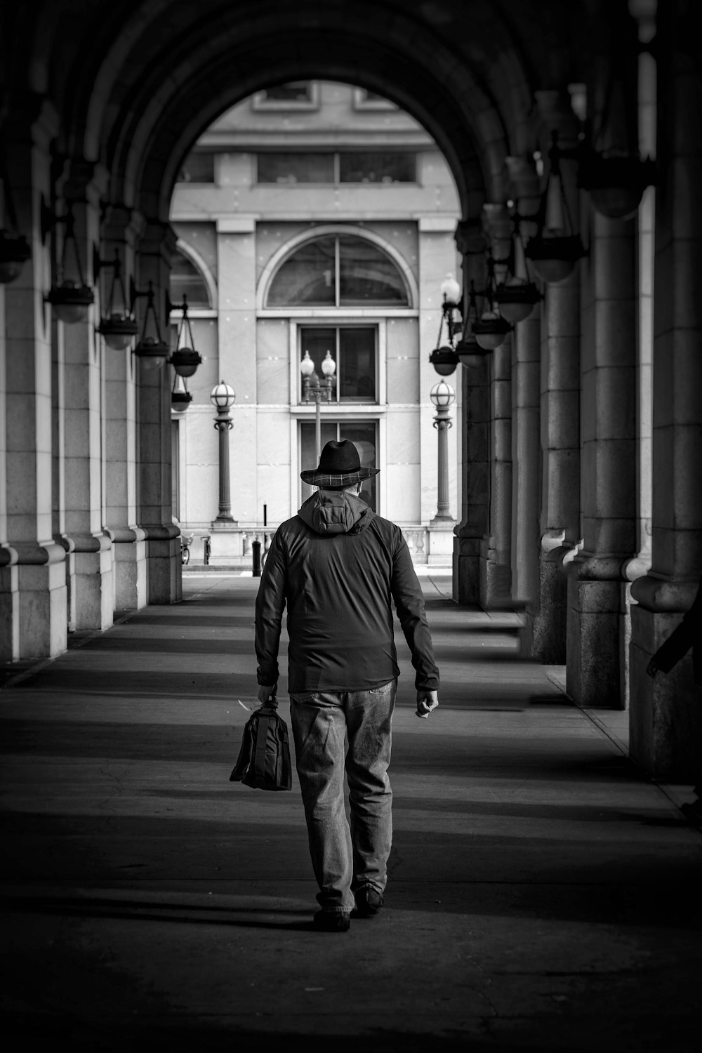 man in black jacket and pants standing on sidewalk in grayscale photography