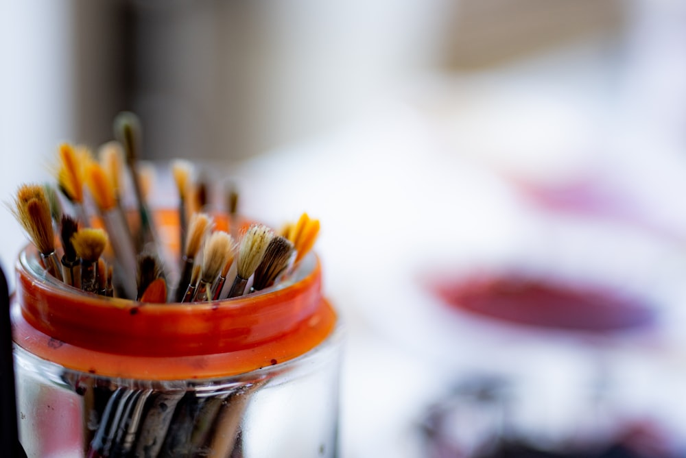 selective focus photography of paint brushes in clear glass jar
