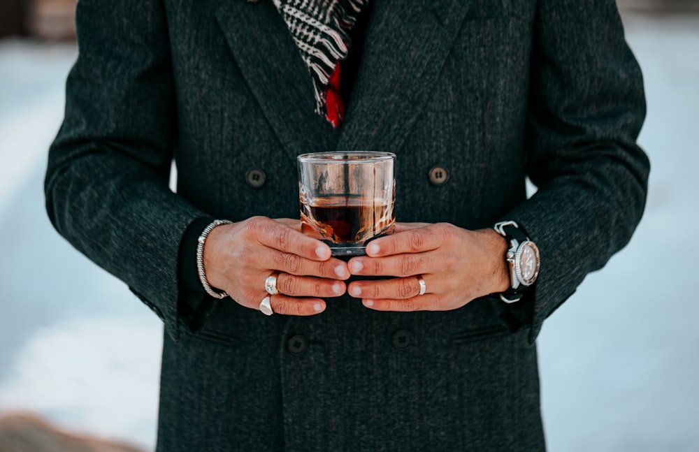 man in black suit holding clear drinking glass