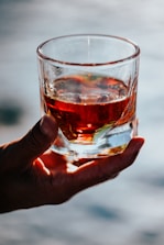 Hands holding a glass of clear spirit with a warm, inviting background.