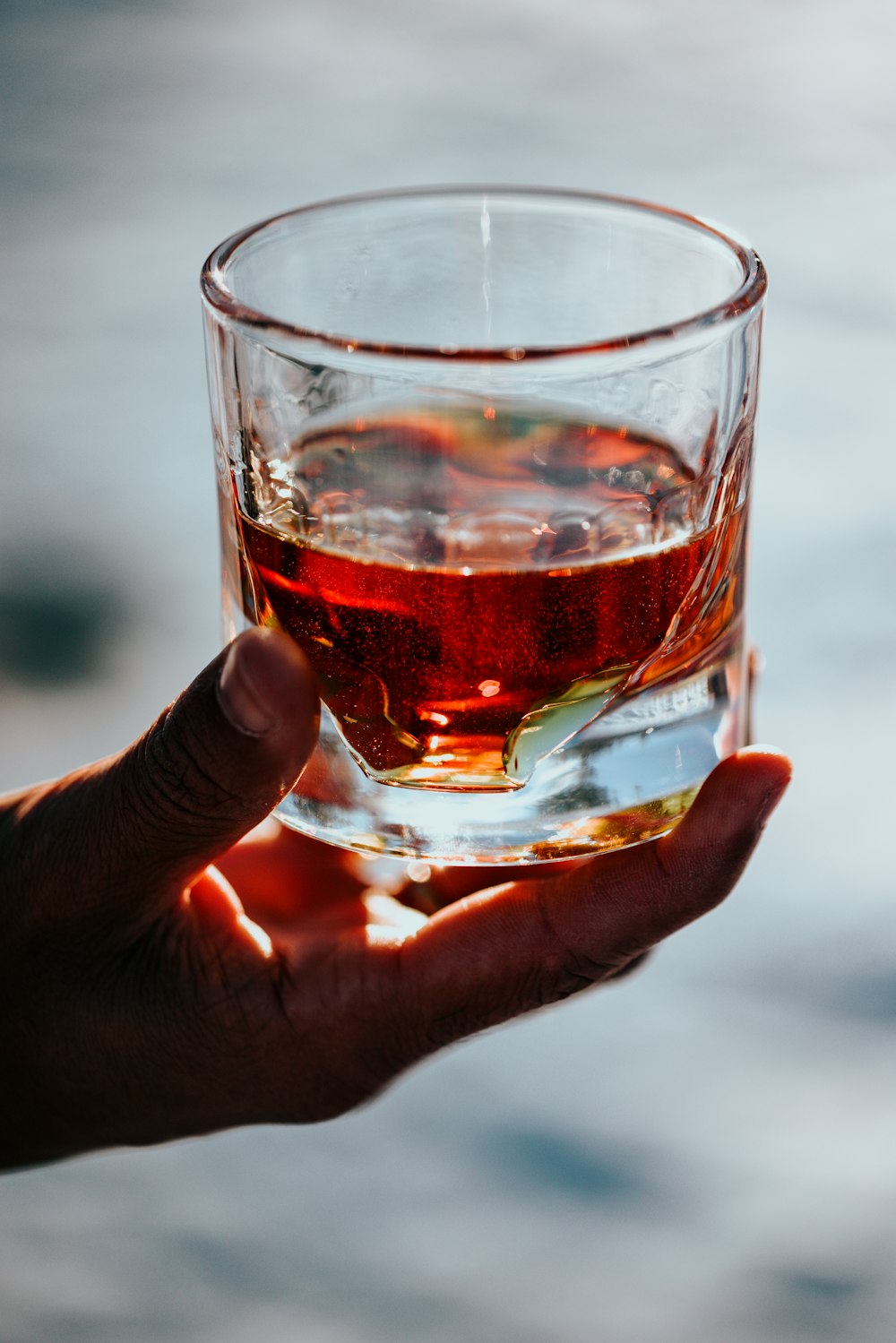 person holding clear drinking glass with red liquid