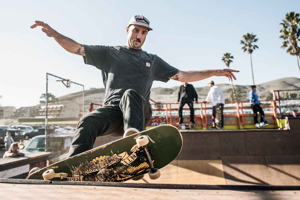 Mann in schwarzem Rundhals-T-Shirt und schwarzer Hose, der tagsüber auf dem Skateboard sitzt