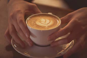 Close-up of hands gently holding a handcrafted ceramic coffee cup on a wooden table.