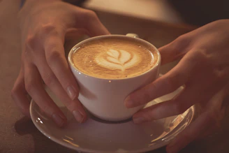 Close-up of gentle hands holding a steaming cup of coffee on a wooden table.