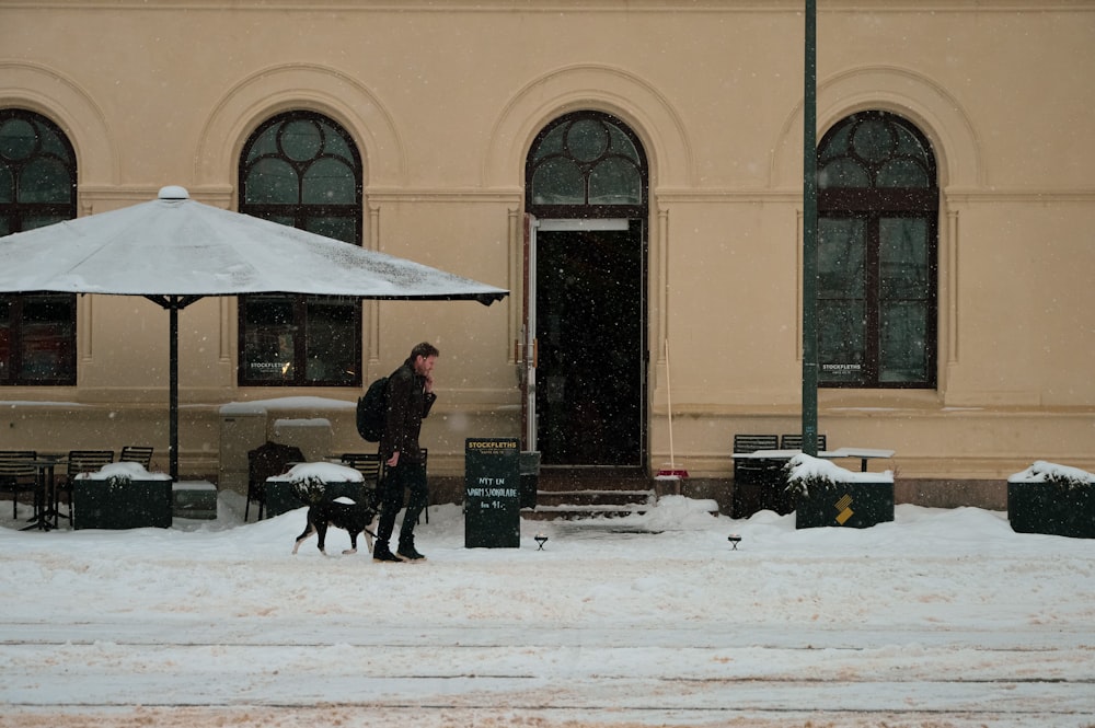 man in black jacket and pants holding white umbrella walking on snow covered ground during daytime