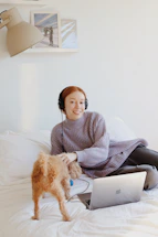 A cheerful pet owner chatting with customer support on a laptop surrounded by colorful pet clothes