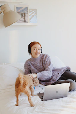 A cheerful pet owner chatting with customer support on a laptop surrounded by colorful pet clothes