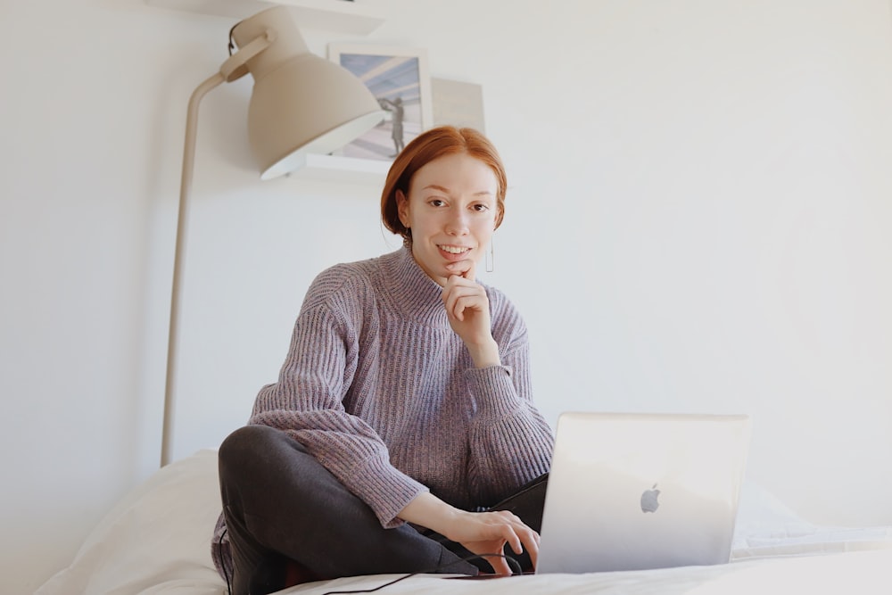 회색 스웨터를 입은 여자가 맥북을 사용하여 의자에 앉아 있다