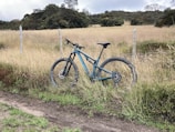 Mountain bike resting against a wooden fence with green hills in the background.