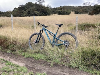 Mountain bike resting against a wooden fence with green hills in the background.